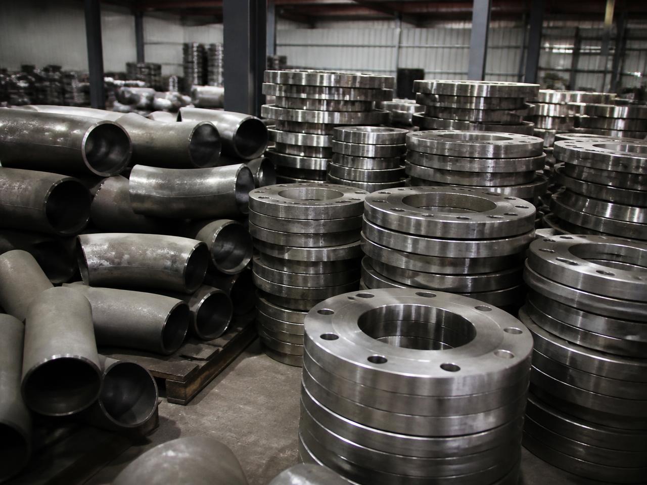 Stacked steel pipe fittings and flanges in an industrial warehouse